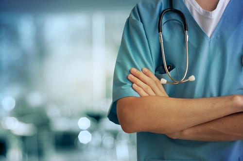 Clinician in blue scrubs with a stethoscope, standing with arms crossed